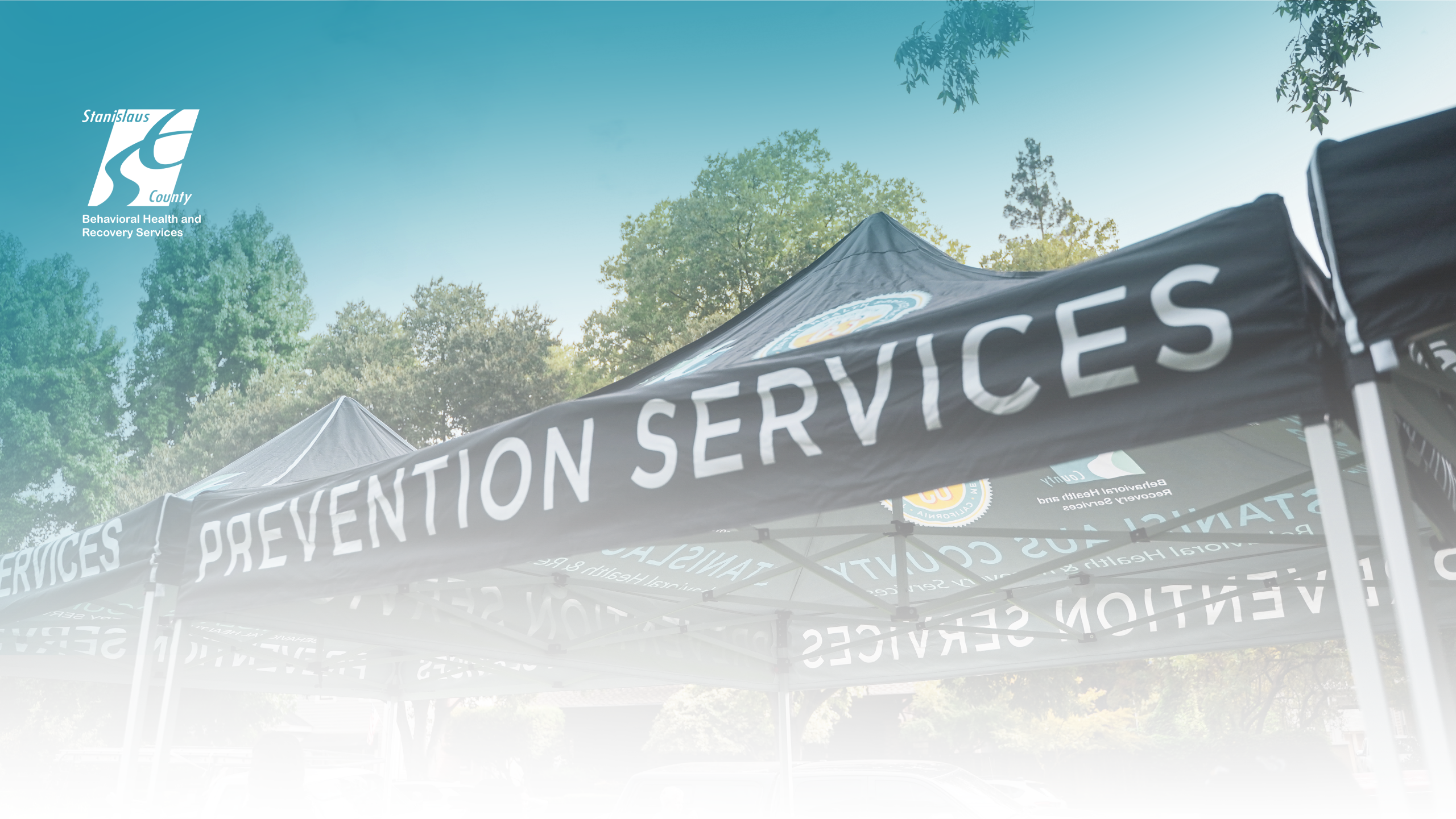 Outdoor event tents with the words “Prevention Services,” set among trees on a sunny day.