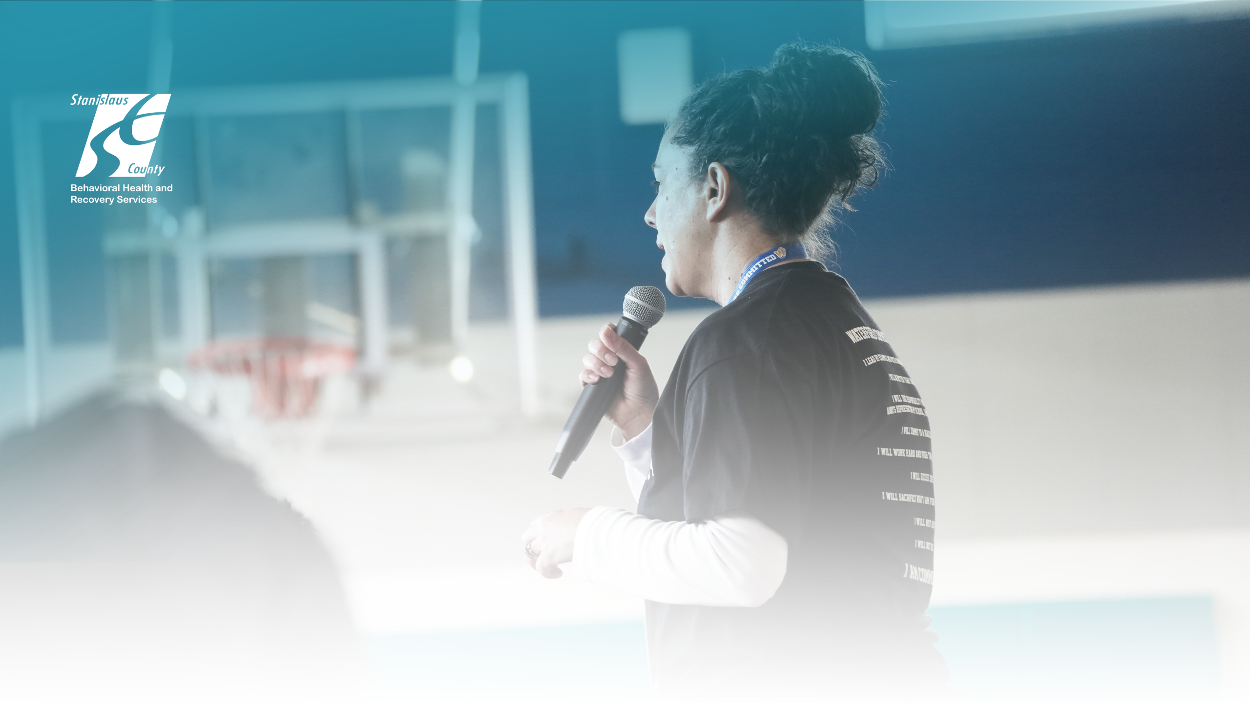 Person speaking into a handheld microphone at an indoor conference event.